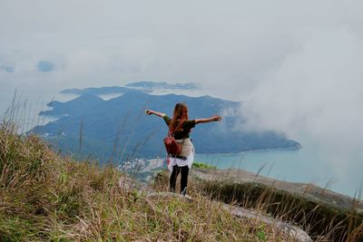 Rear view of woman standing on mountain against sky