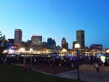 Crowd at illuminated city against clear blue sky