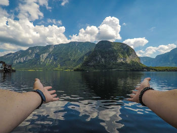 Cropped image of hand on lake against mountain range