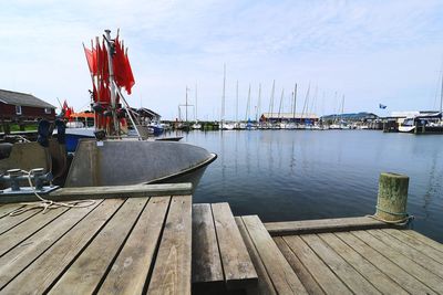 Sailboats moored on pier at harbor against sky