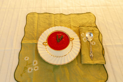 Tomato soup in a white and gold bowl on an embroidered green placemat.
