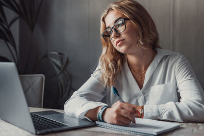 Portrait of young woman using laptop while sitting in office