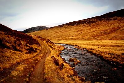 Dirt road leading towards mountain against sky