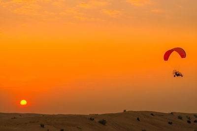 Silhouette person paragliding at sunset