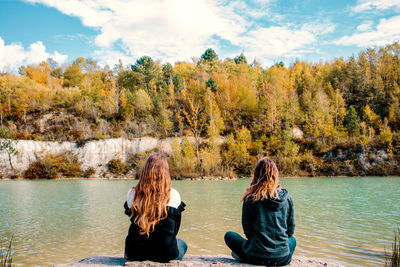 Rear view of two women sitting by lake against mountain