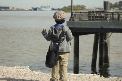 Rear view of boy gesturing while standing at beach