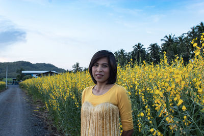 Portrait of woman standing against yellow flowering plants