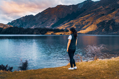 Rear view of woman standing by lake against mountains