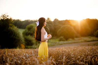 A girl runs through a field with spikelets against the background of the setting sun