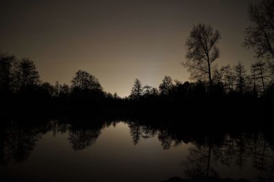 Reflection of silhouette trees in lake against sky at night