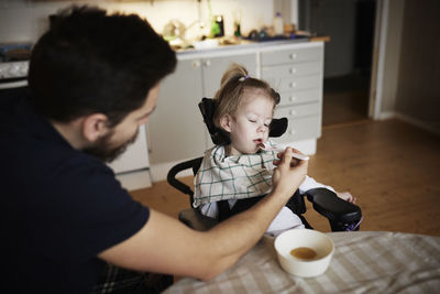 Father feeding disabled child in wheelchair at home