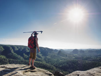 Hiker with red backpack greetings the world with arm rised up head with trekking stick. man alone