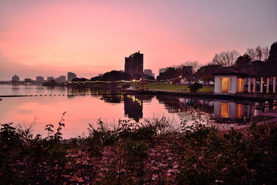 Scenic view of lake by buildings against sky during sunset