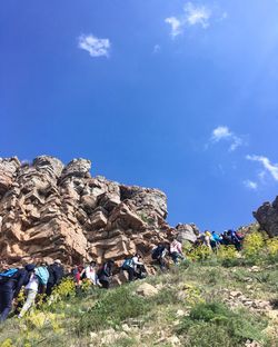 Low angle view of people on rock against blue sky