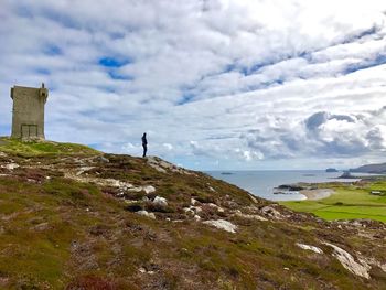 Man standing on rock by sea against sky