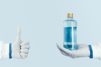 Close-up of hand holding bottle against white background