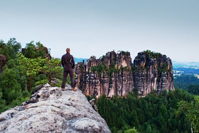 Rear view of man standing on rock against sky