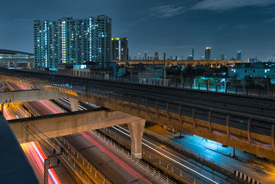 Illuminated railroad tracks by buildings against sky at dusk