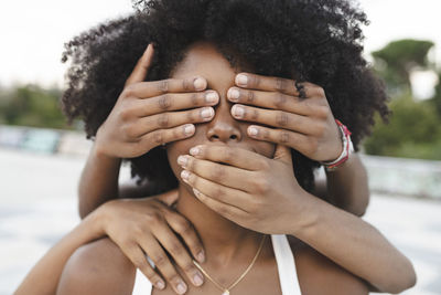 Young female friends covering mouth and eyes of afro woman