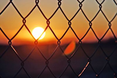 Close-up of chainlink fence against sunset sky