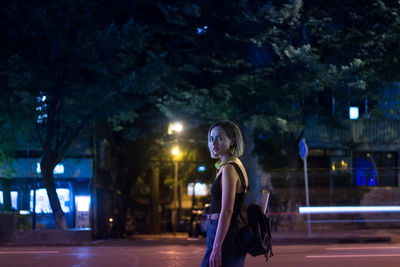 Portrait of woman standing by illuminated street at night