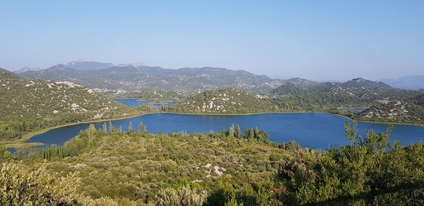 Scenic view of lake and mountains against clear blue sky