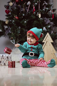 A little 12-month-old christmas elf with a christmas tree and gifts