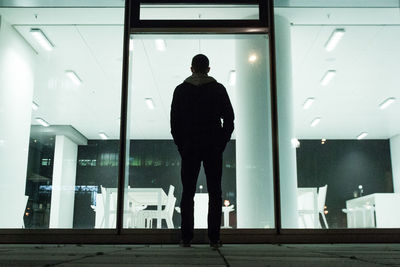 Rear view full length of man standing against glass window in building