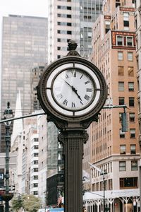 Low angle view of clock on street amidst buildings in city