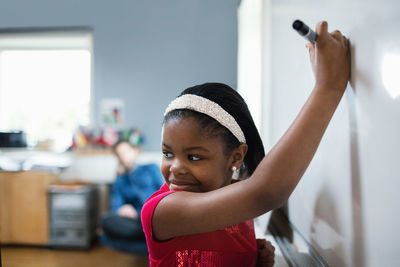 Close-up of girl looking over shoulder while writing on whiteboard in classroom