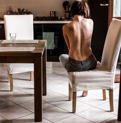Rear view of shirtless man sitting on chair at home