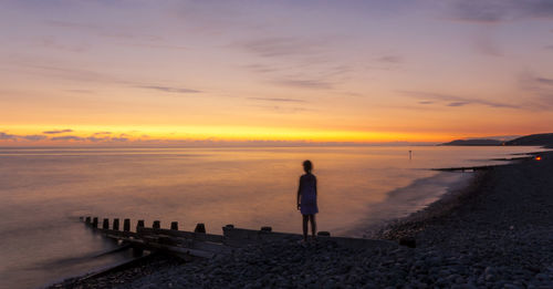 Rear view of woman standing on beach against sky during sunset