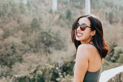 Portrait of young woman wearing sunglasses standing against trees