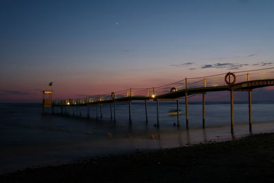 Illuminated bridge over sea against sky during sunset