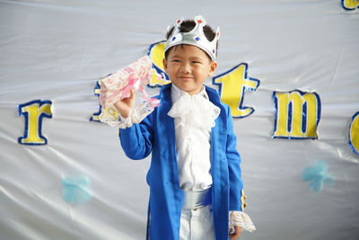 Smiling boy wearing crown holding gift box while standing in party