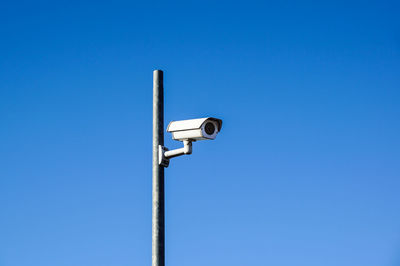 Low angle view of security camera on pole against clear blue sky