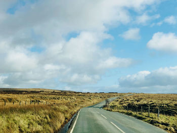 Empty road amidst field against sky