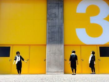 Full length rear view of man walking on yellow wall