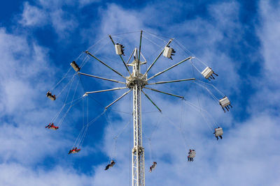 Low angle view of people on chain swing ride against cloudy sky