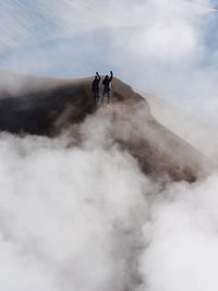 Friends standing on mountain against cloudy sky