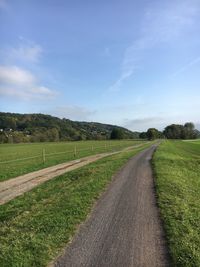 Empty road amidst field against sky