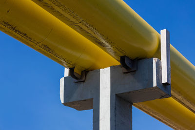 Low angle view of yellow pipe against clear blue sky