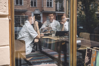 Male and female chefs discussing at restaurant table seen through glass window