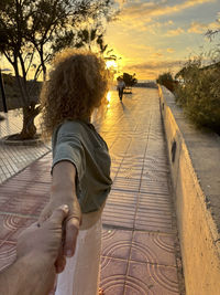 Rear view of woman standing on footbridge against sky during sunset