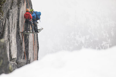 Two climbers standing on portaledge, setting up camp for night.