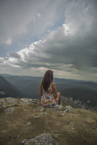 Rear view of woman sitting on mountain against sky