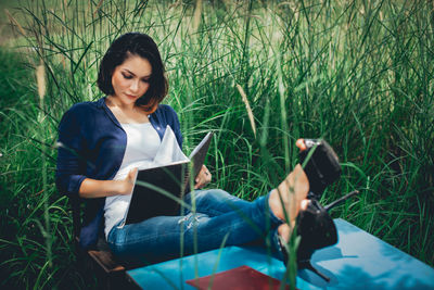 Young woman reading book while sitting against plants