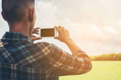 Rear view of man photographing through smart phone against sky