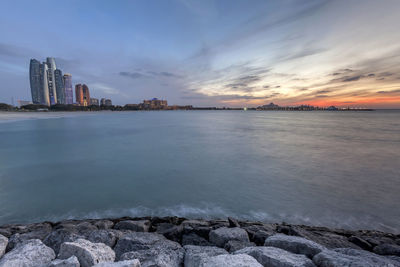 Scenic view of sea by buildings against sky during sunset