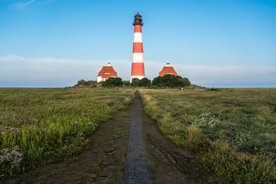 Lighthouse by field against sky